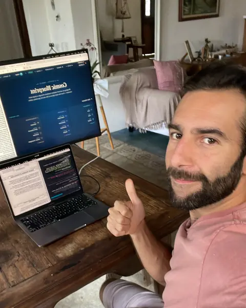 Felipe na mesa de trabalho com o Cosmic Codex no notebook, o gato no colo.